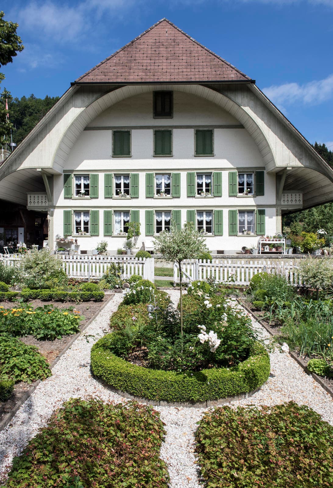 Emmentaler Bauernhaus der Familie Bracher mit weisser Holzfassade und grünen Fensterläden. Im Vordergrund der Garten.