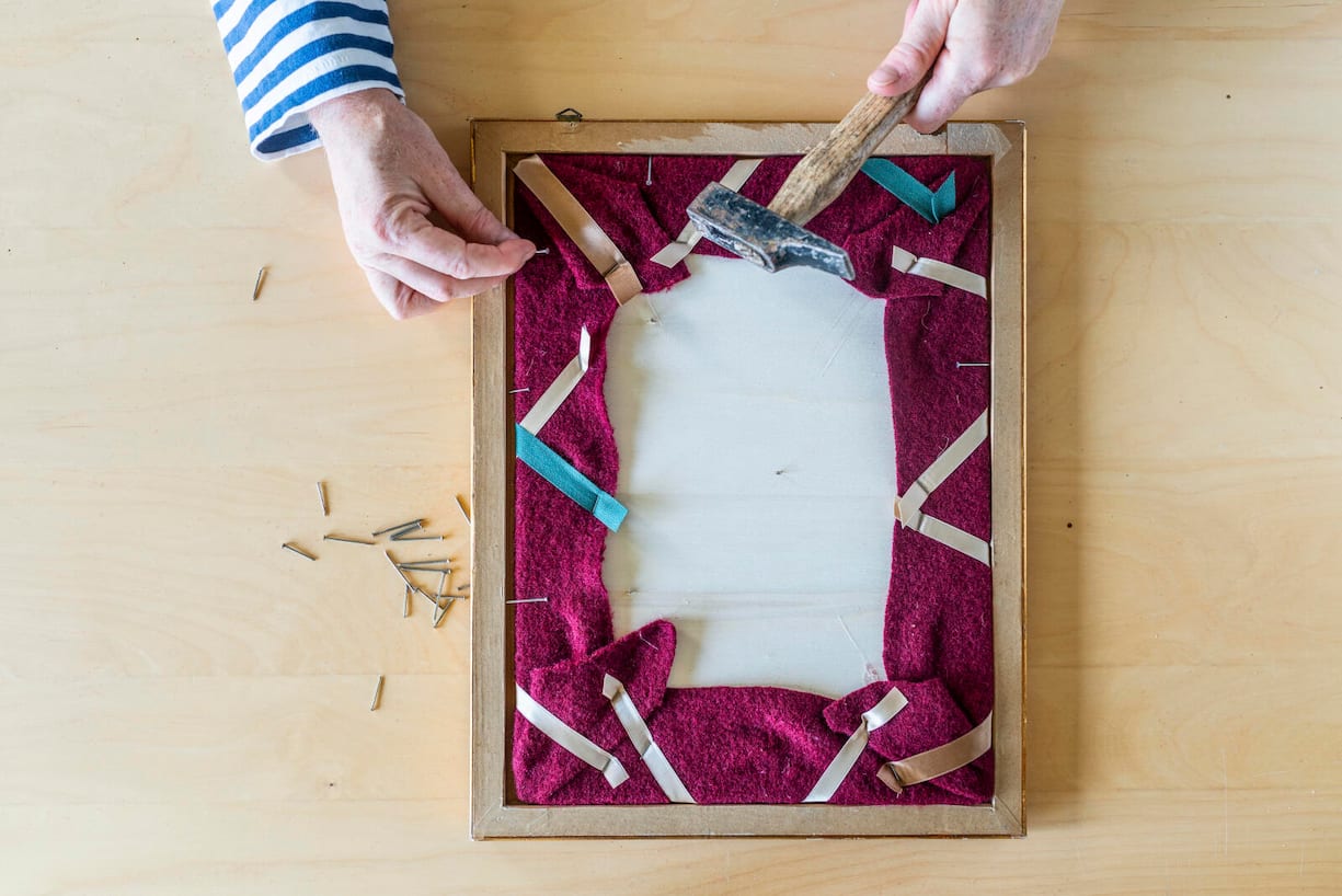 Holzplatte wird mit Hammer und Nägeln auf dem Rahmen fixiert