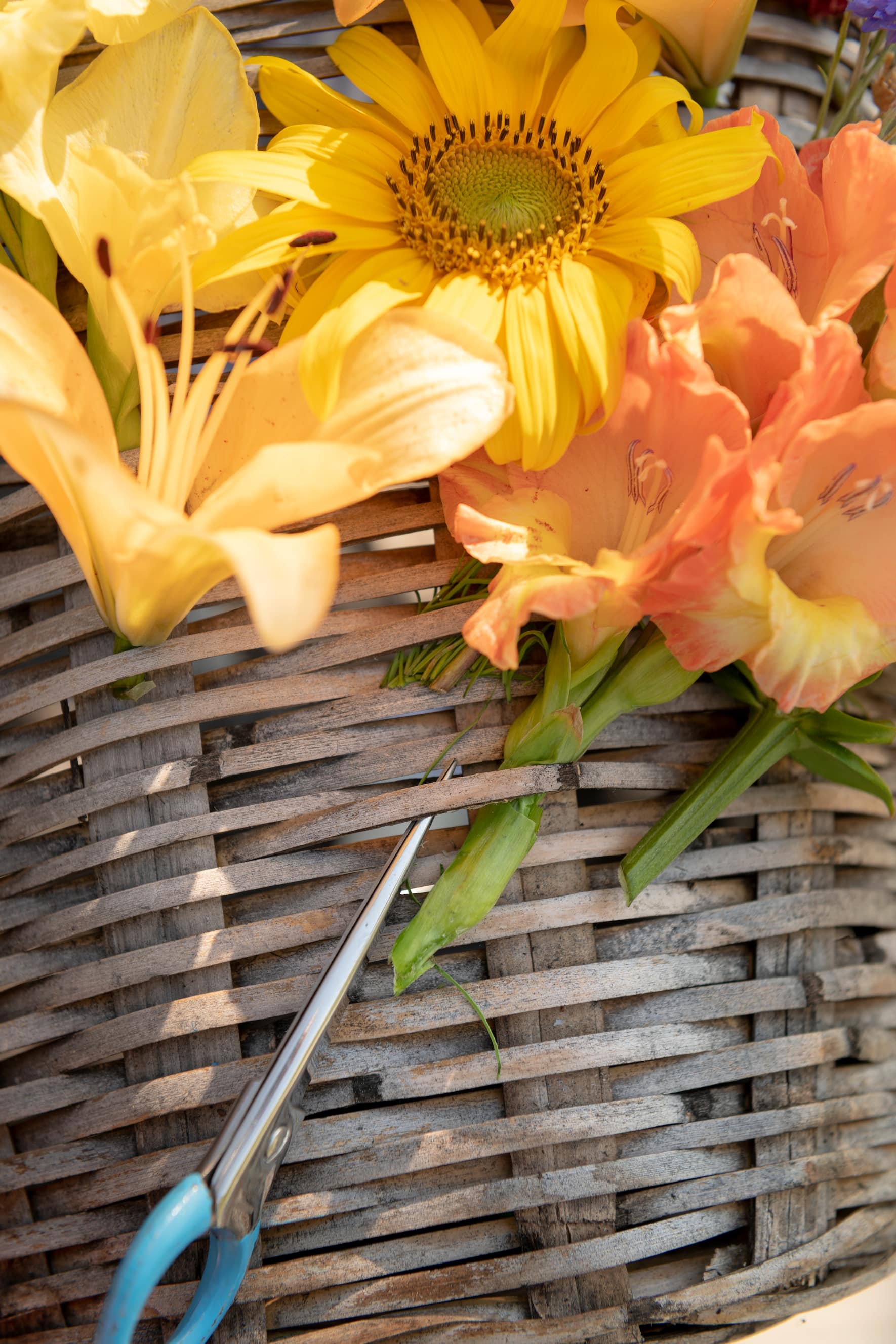 Flechtkorb mit gelben und orangen Blumen und einer hellblauen Schere