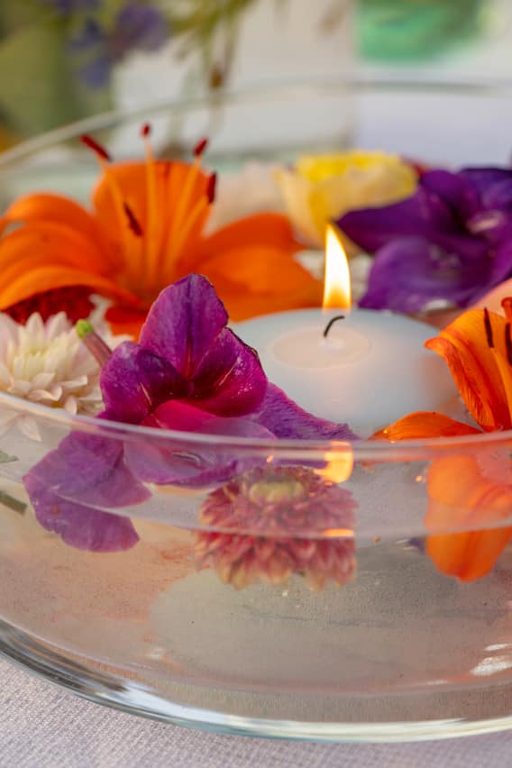 Flaches Gefäss mit bunten Blumen im Wasser und einer angezündeten Schwimmkerze