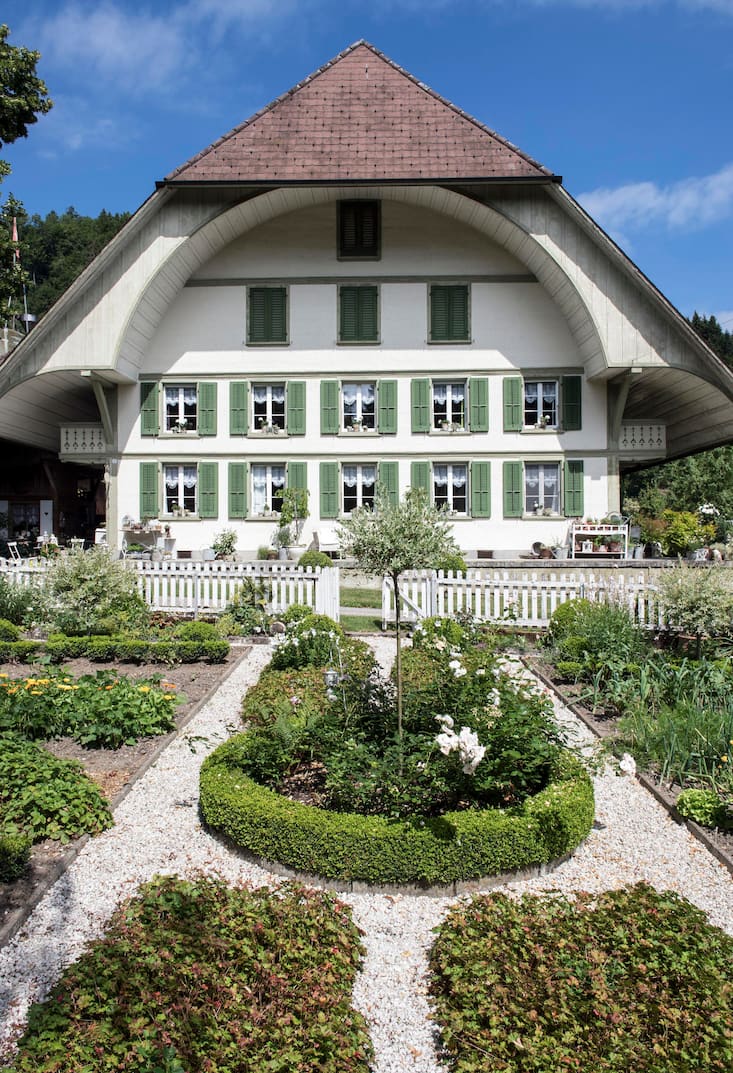 Emmentaler Bauernhaus der Familie Bracher mit weisser Holzfassade und grünen Fensterläden. Im Vordergrund der Garten.
