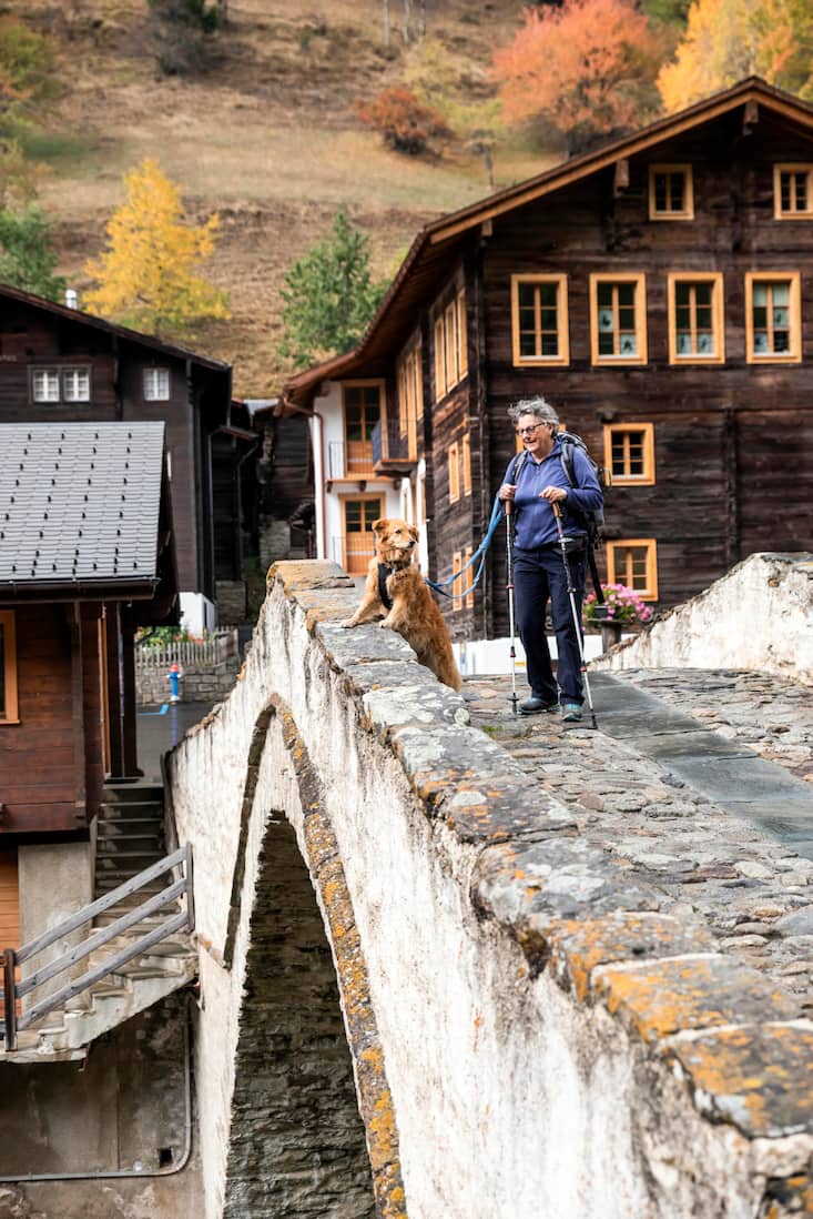 Mischlingshündin Tapas und Chefin Christine Nydegger wandern über die Brücke über die Binna im Dorf Binn VS