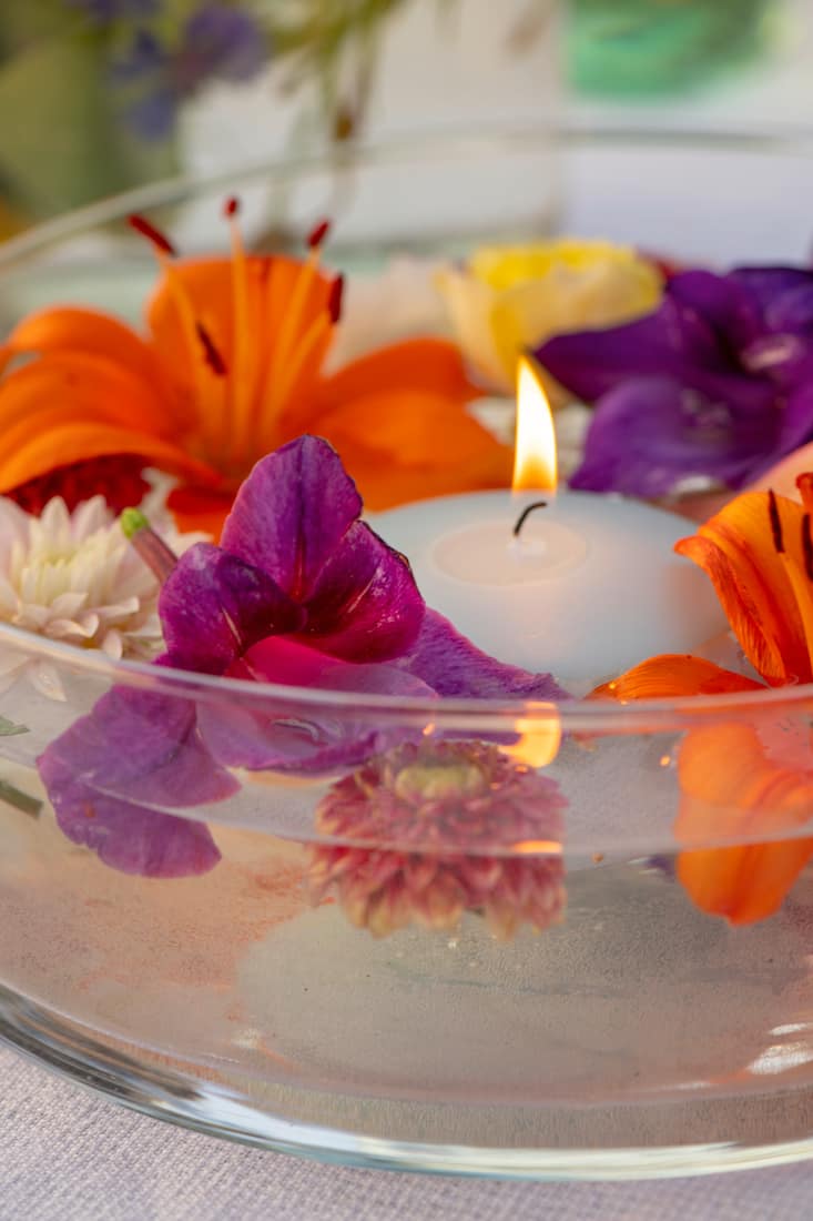 Flaches Gefäss mit bunten Blumen im Wasser und einer angezündeten Schwimmkerze