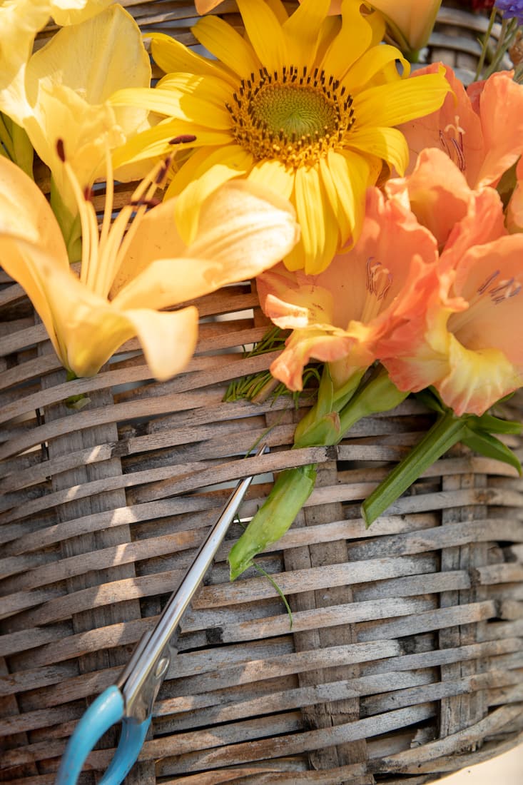 Flechtkorb mit gelben und orangen Blumen und einer hellblauen Schere