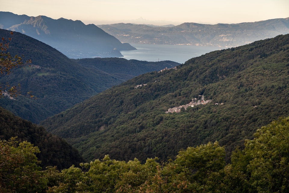 Blick auf das Schweizer Bergdorf Indemini im Hang, umgeben von Wald